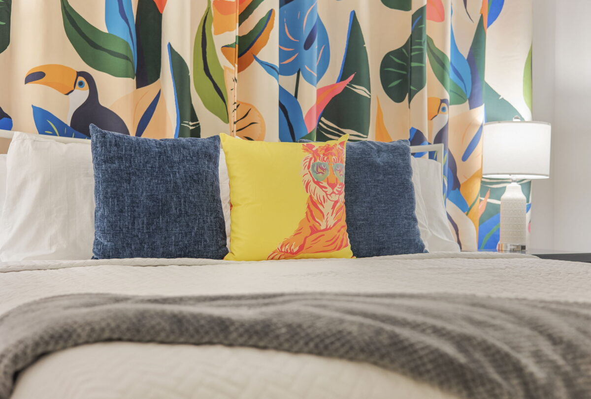 Bed dressed in yellow and blue cushions against a tropical leaf mural