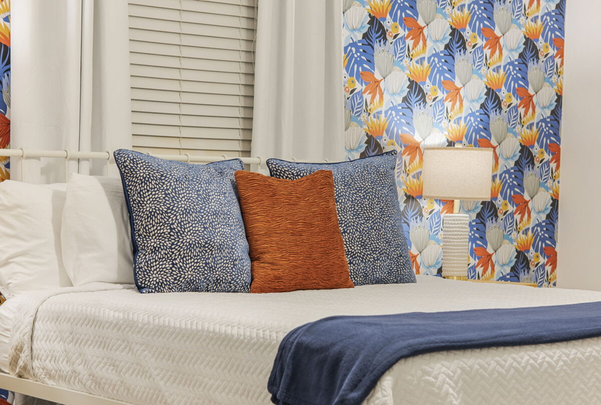 Bed with patterned cushions against bright botanical wallpaper