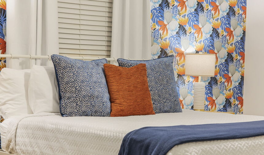 Bed with patterned cushions against bright botanical wallpaper