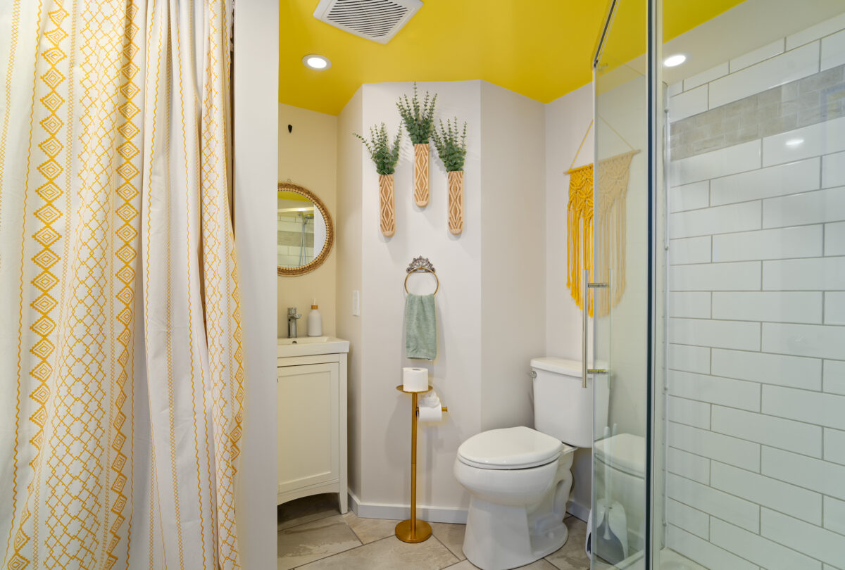 Bathroom with a yellow accent wall, round mirror and glass shower