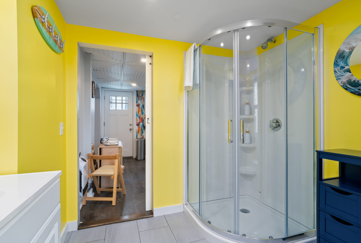 Hallway with a yellow accent wall leading to a corner shower