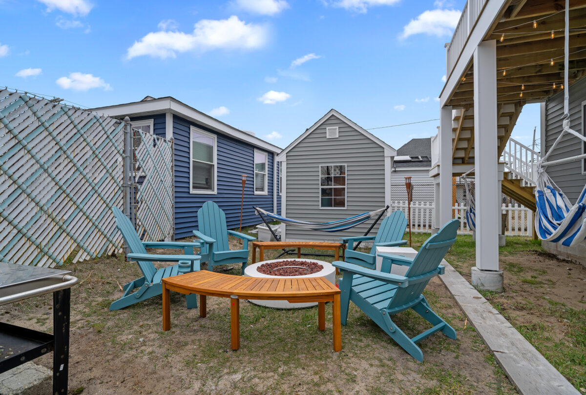 Backyard fire pit with teal Adirondack chairs between two houses