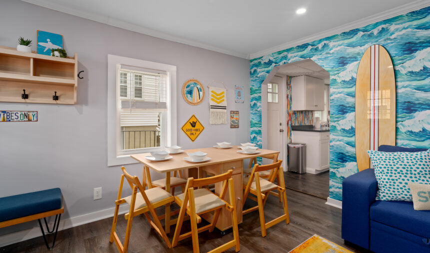 Dining area with wooden chairs beside an ocean-wave feature wall