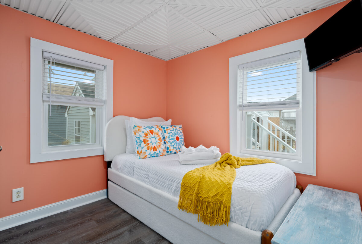 Bedroom with coral walls, white bedding and a mustard throw