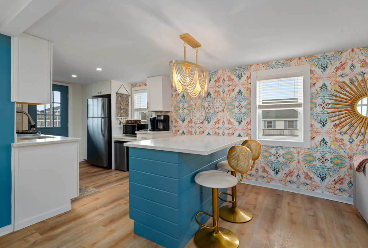 Kitchen with a teal island, gold bar stools and patterned wallpaper