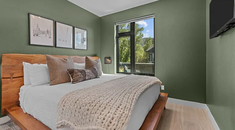 Bedroom with sage walls, layered neutral bedding and coastal prints