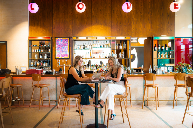 Hotel bar with two guests at a high table and shelves of bottles