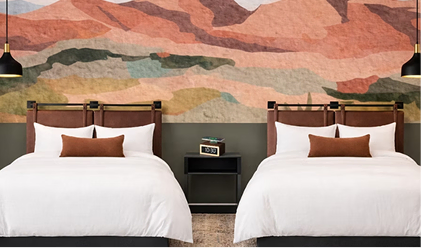Two hotel beds beneath a layered desert landscape mural