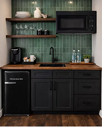 Kitchenette with a green tiled splashback and a black mini fridge