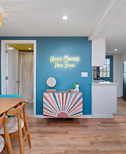 Entryway with a sunburst console and a neon Here Comes The Sun sign