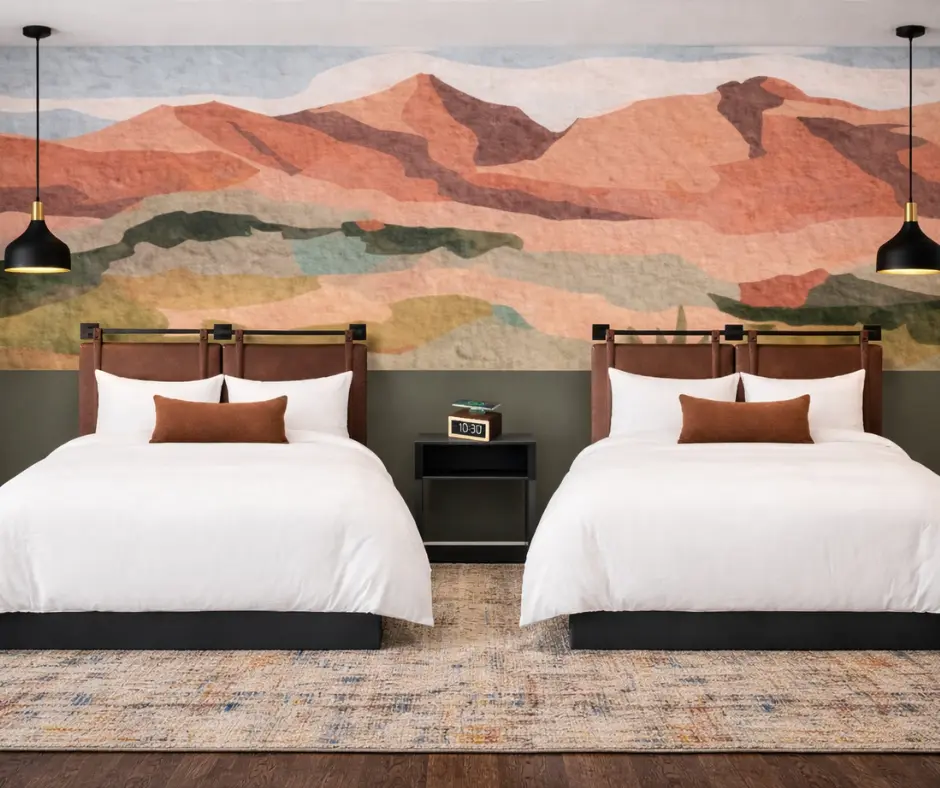 Two hotel beds beneath a layered desert landscape mural