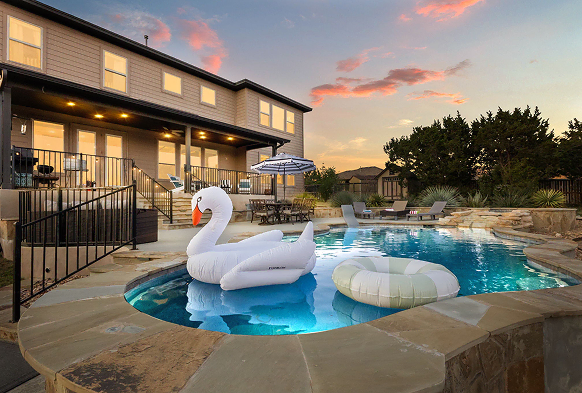 Swimming pool with inflatable floats at sunset behind a house