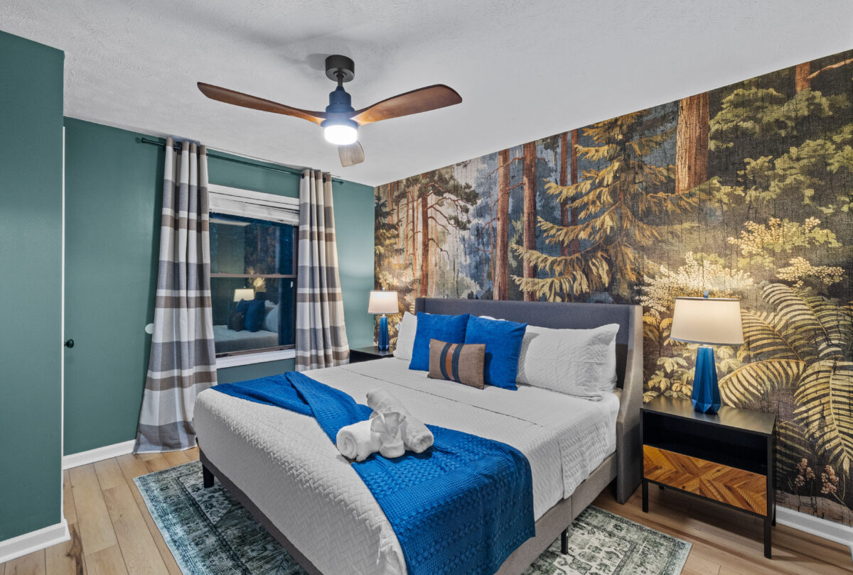 Bedroom with a forest mural, blue bedding and a ceiling fan