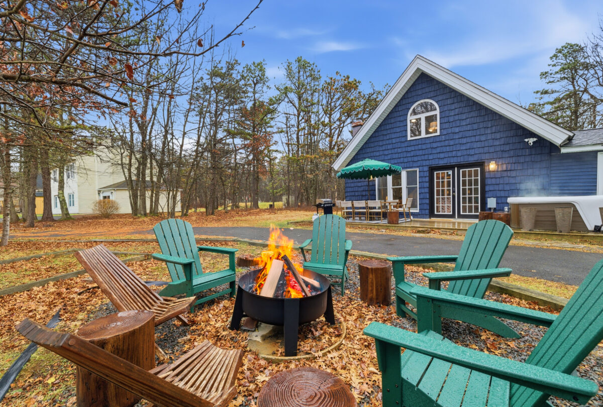 Evening fire pit with Adirondack chairs in front of a blue cottage