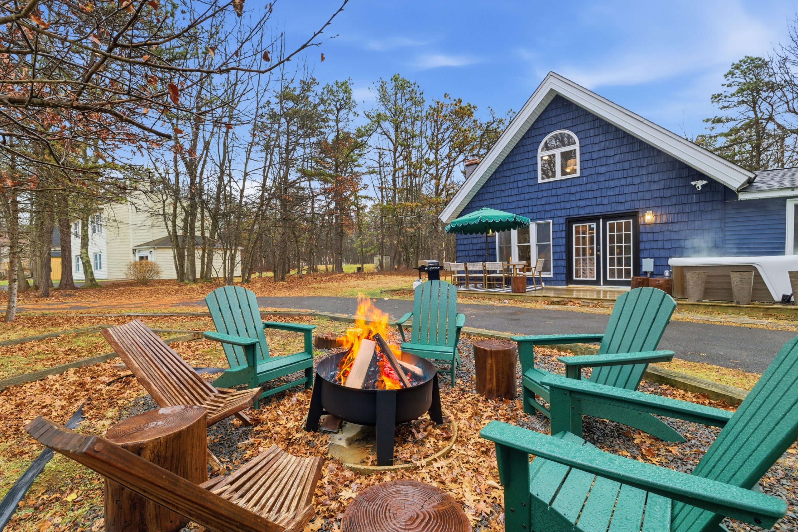 Evening fire pit with Adirondack chairs in front of a blue cottage