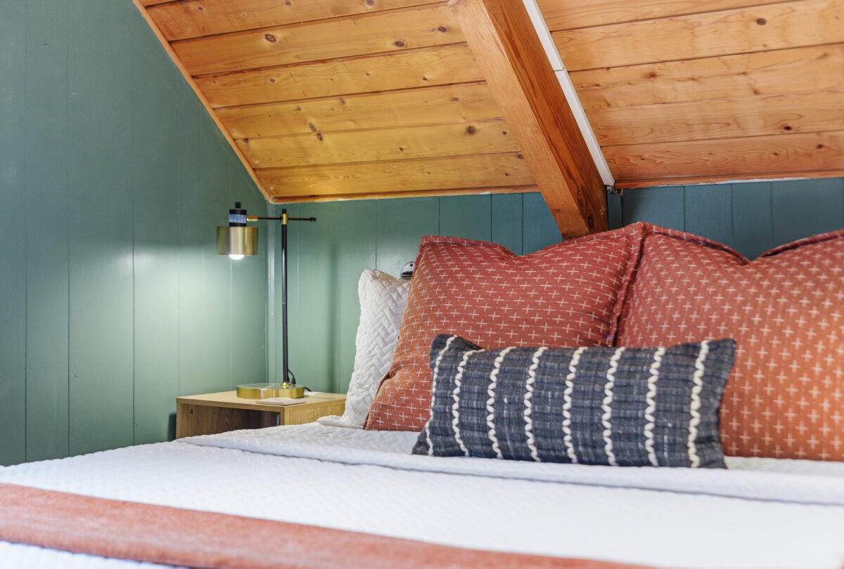 Bed under a timber A-frame ceiling with sage panelling and rust cushions
