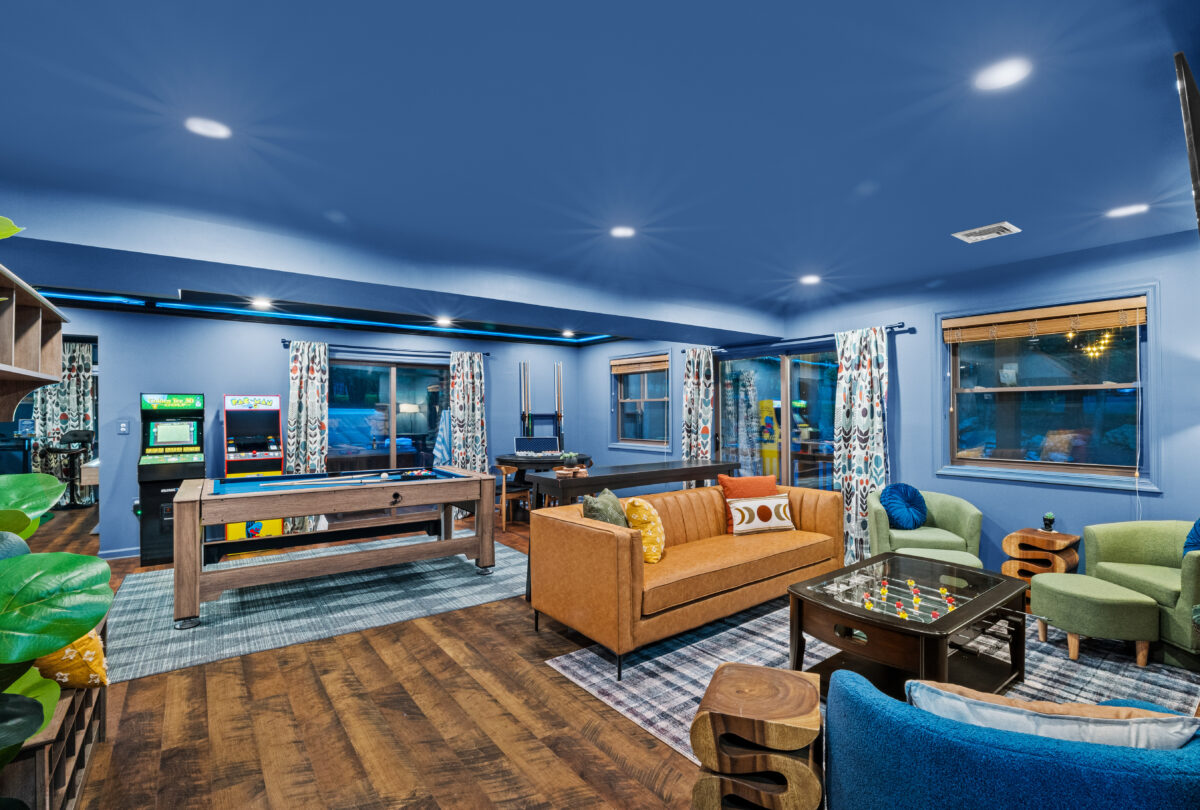 Open-plan lounge with a tan sofa, blue ceiling and shuffleboard table