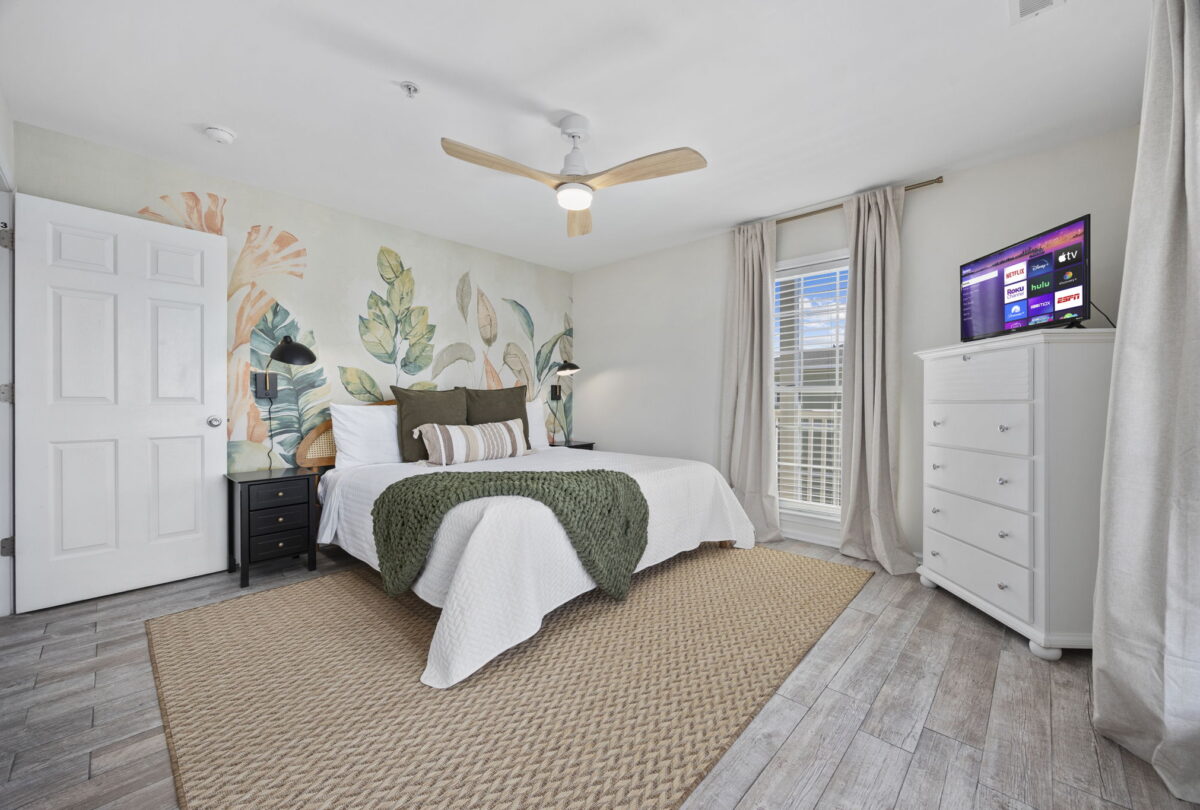 Bedroom with a botanical mural, green bedding and a ceiling fan