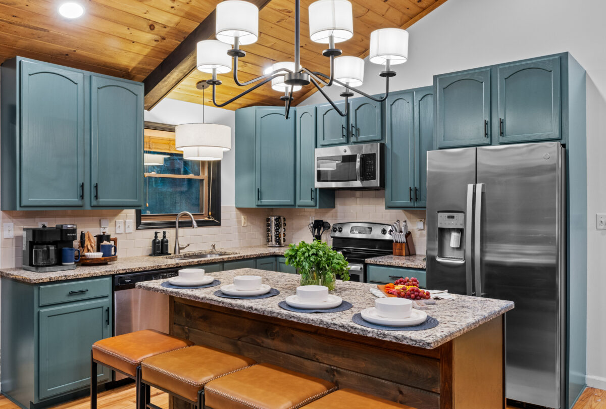 Kitchen with sage cabinets, a granite island and orange stools
