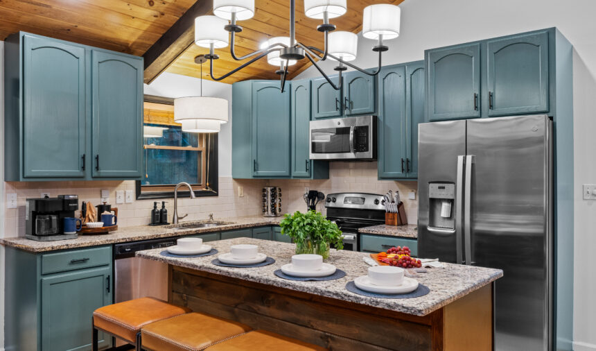 Kitchen with sage cabinets, a granite island and orange stools