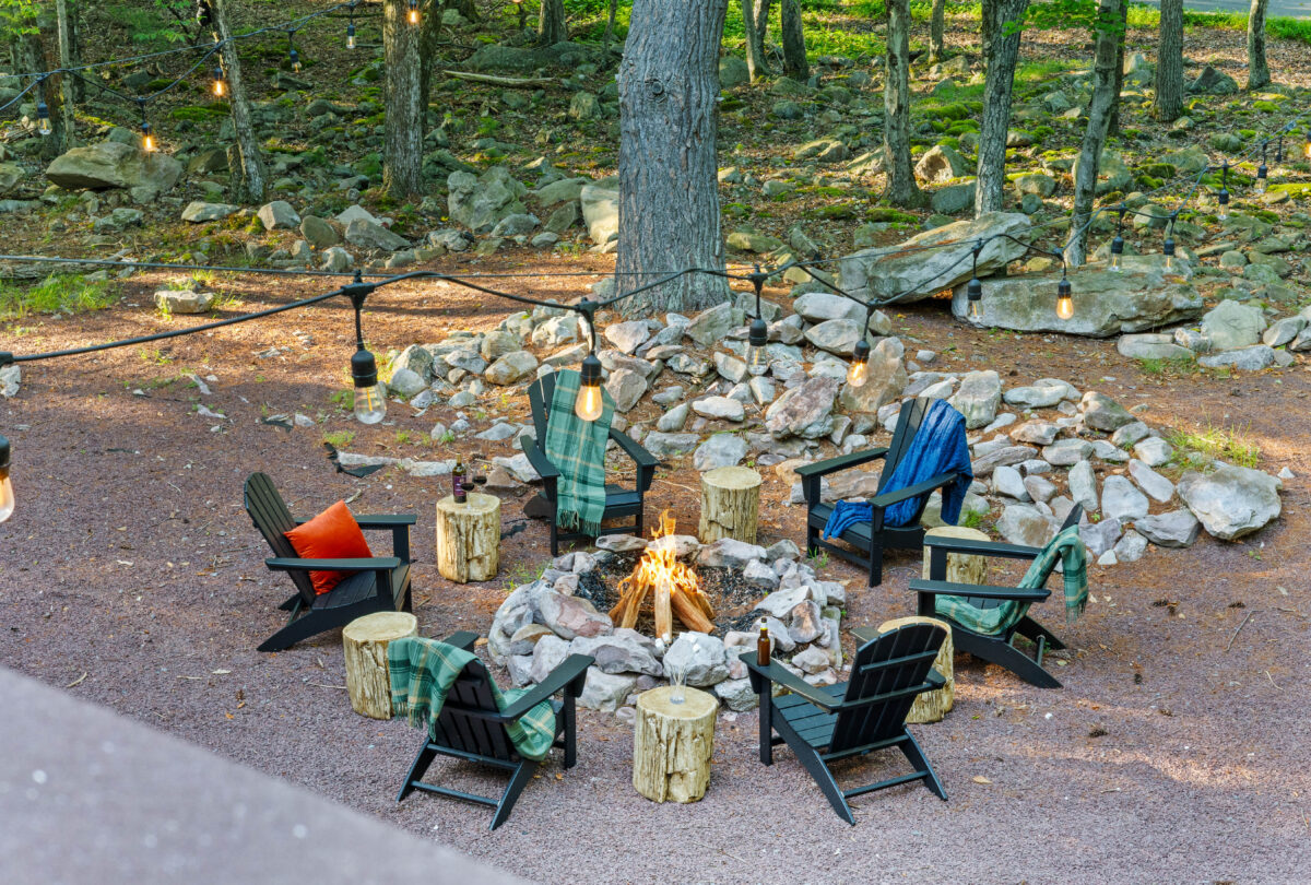 Evening fire pit with log stools and Adirondack chairs in the woods