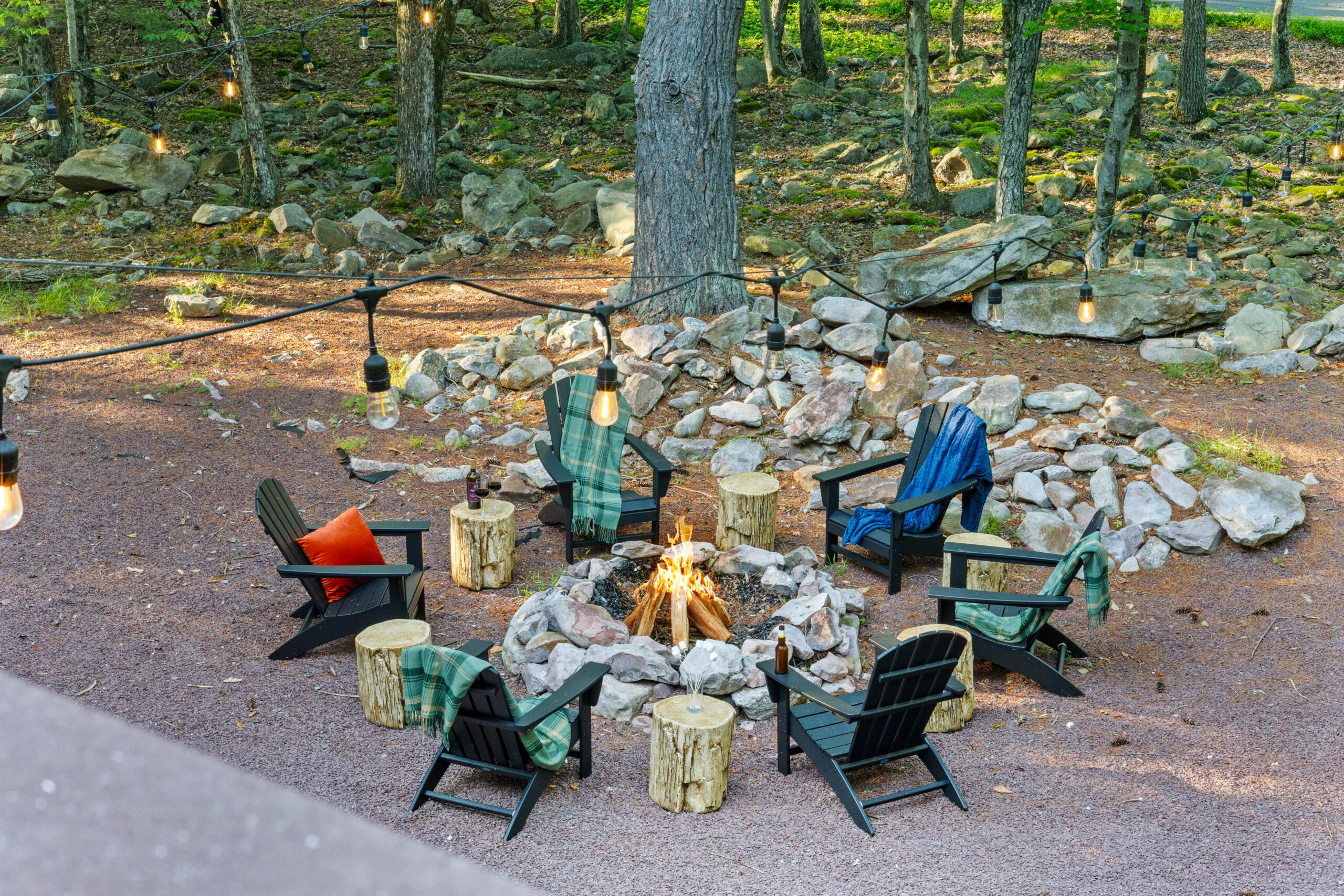 Evening fire pit with log stools and Adirondack chairs in the woods