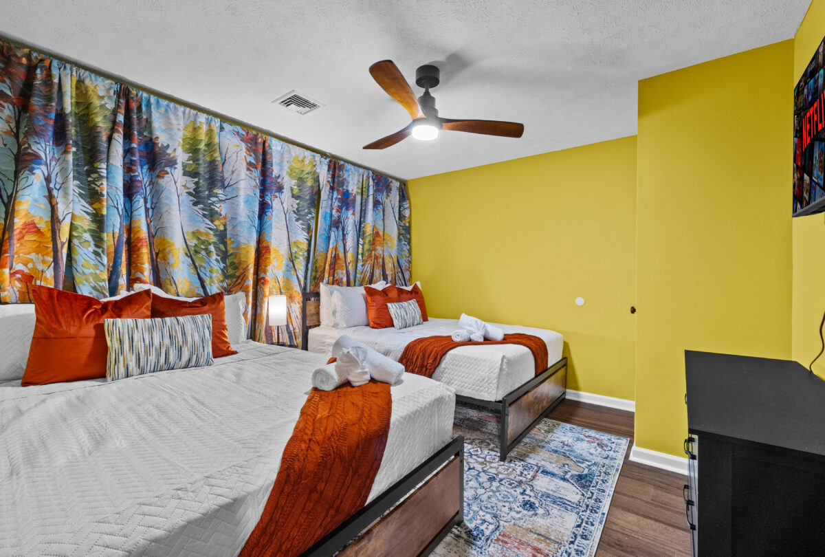 Bedroom with two beds, a yellow accent wall and botanical curtains