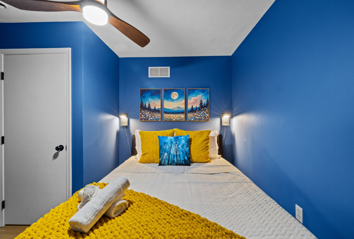 Bedroom with cobalt walls, mustard bedding and framed moon prints