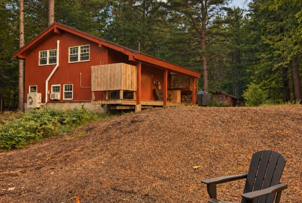 Red-stained chalet among the pines with a fire pit in the foreground
