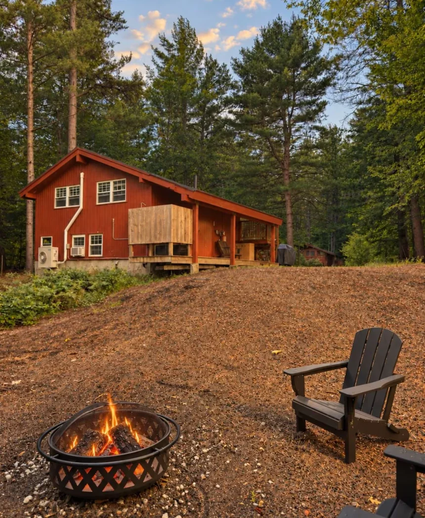 Red-stained chalet among the pines with a fire pit in the foreground