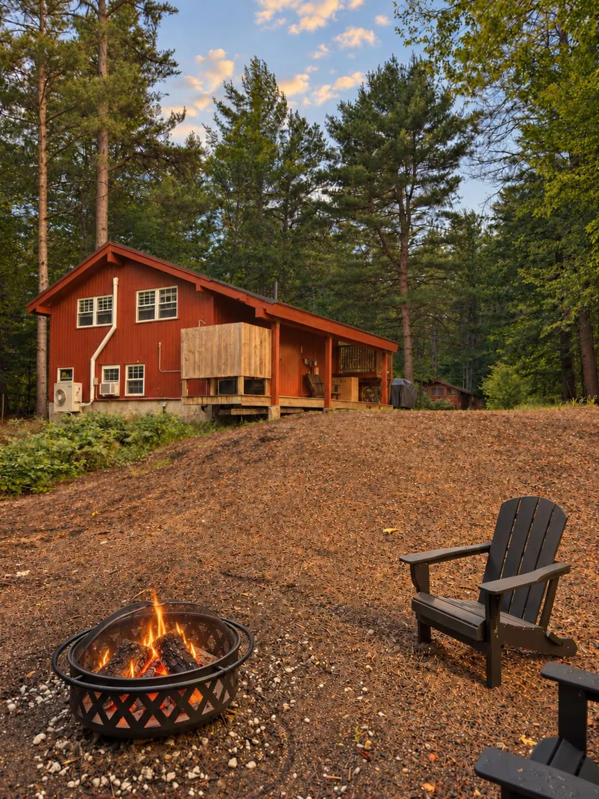 Red-stained chalet among the pines with a fire pit in the foreground