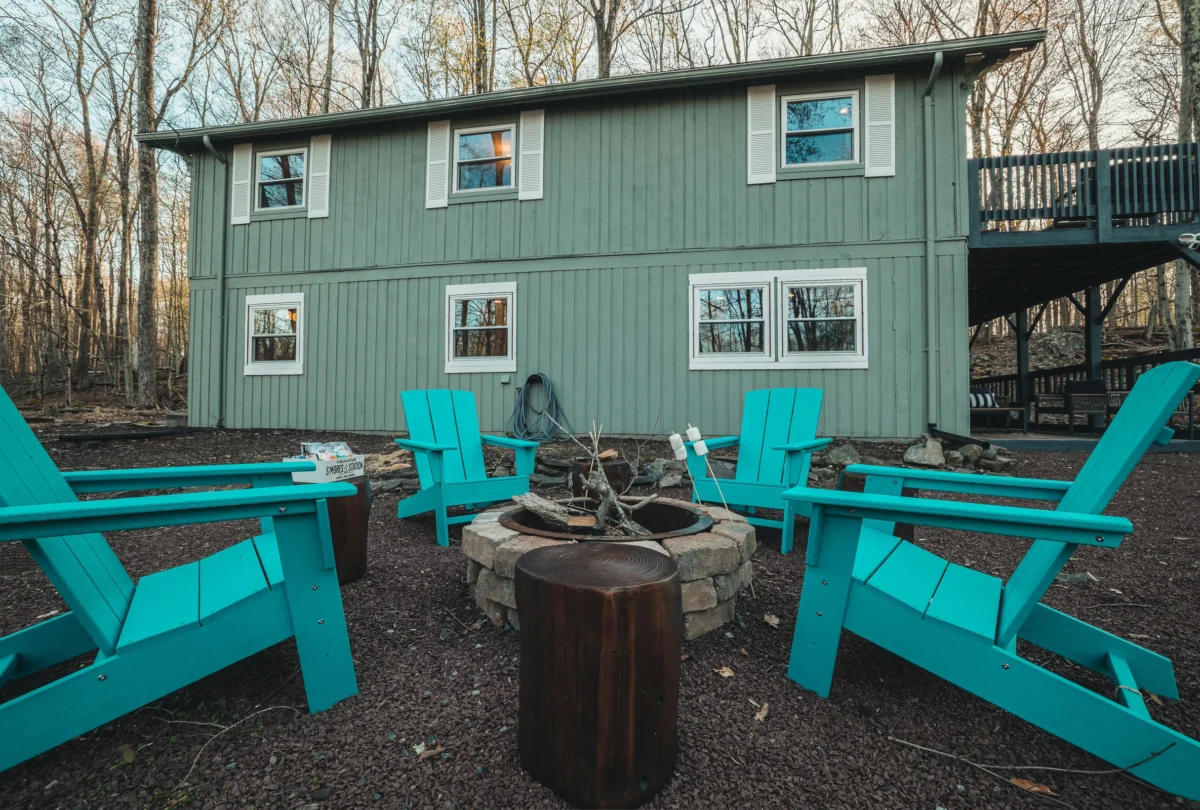 Fire pit ringed by teal Adirondack chairs outside the cabin