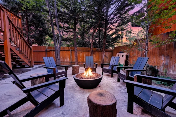 Fire pit burning among the trees, ringed by Adirondack chairs