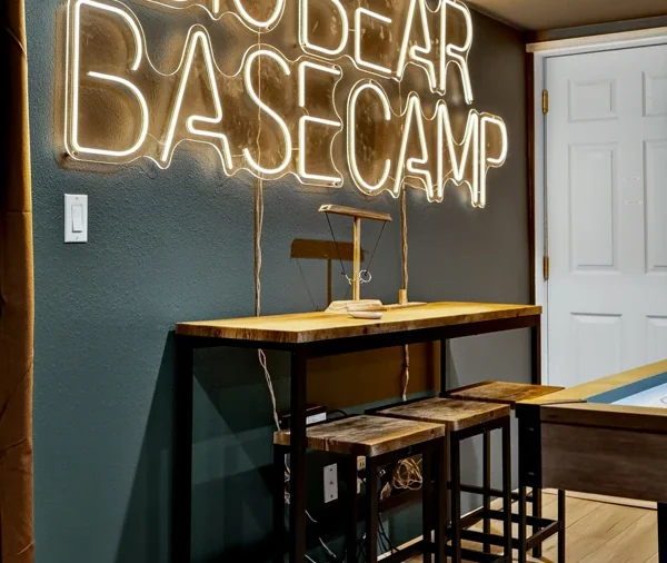 Games room with a neon sign reading Big Bear Basecamp and bar stools