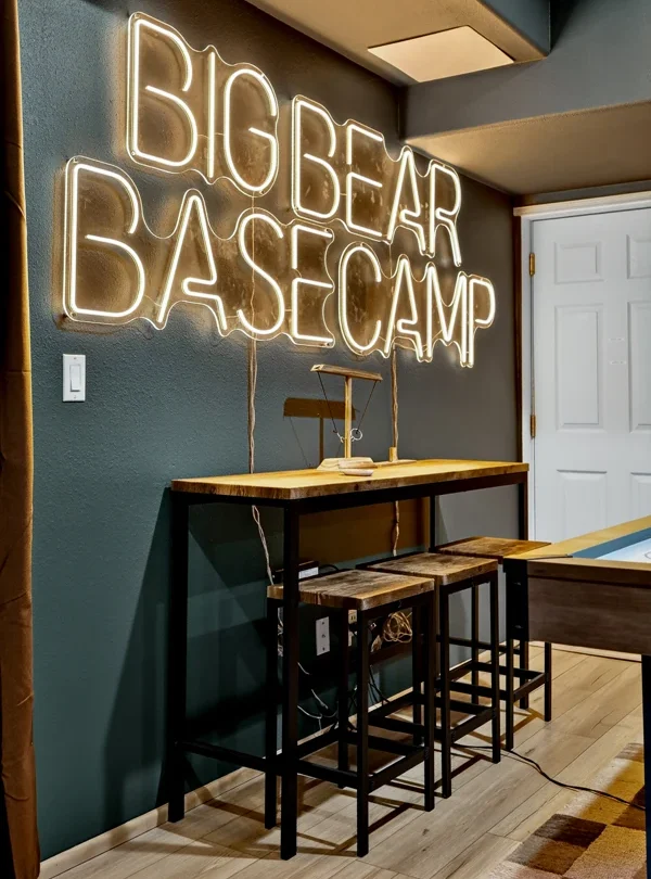 Games room with a neon sign reading Big Bear Basecamp and bar stools