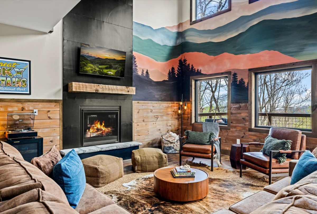Living room with a lit fireplace below a layered mountain mural