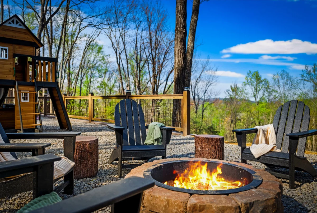 Lit fire pit ringed by Adirondack chairs among the trees